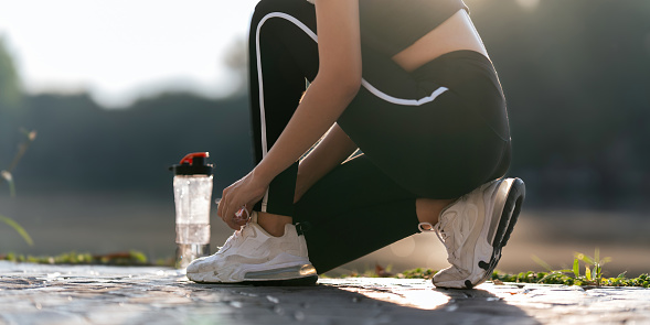 Young woman ties shoelaces while stretching stretch during stretching exercise outdoors in the park.