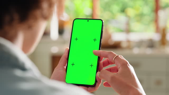 Hands of person, scroll phone and green screen in home, online search or communication. Smartphone, closeup and chroma key, email and internet on social media app, mockup space and tracking markers