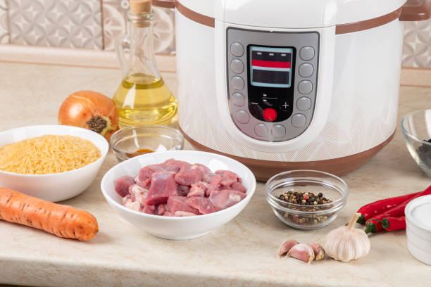 istock Prepared raw ingredients for cooking pilaf in modern multi cooker in kitchen on a table. Cooking pilau with meat in multicooker. 1856697881