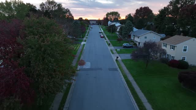 Quaint neighborhood during autumn sunset. Aerial reveal above street lined with houses and homes in USA suburb.