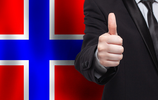 Norwegian concept. Businessman showing thumb up on the background of flag of Norway