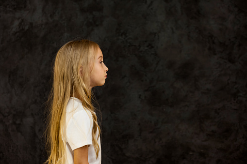 Portrait of side view girl child model in white t-shirt expression emotion, confident looking away. Serious cute kid 6 year old posing at black, studio shot. Kids emotional concept. Copy ad text space
