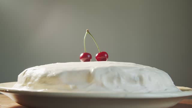 A hand places two fused red cherries on a white cake