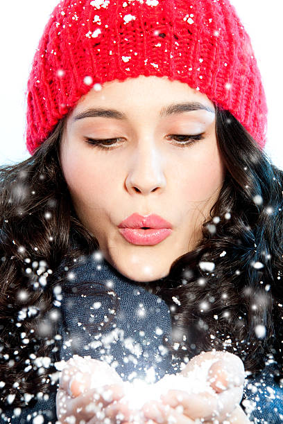 Beautiful young woman blowing snow in hands.