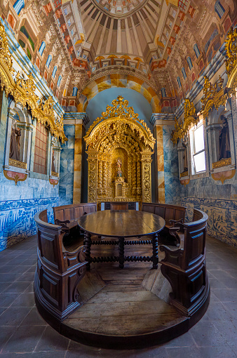 Luxuriously decorated living room with a wooden table, chapel with golden motifs with the statue of Saint Francis, blue tiles and religious sculptures on the walls. Church of Saint Francis. Evora.