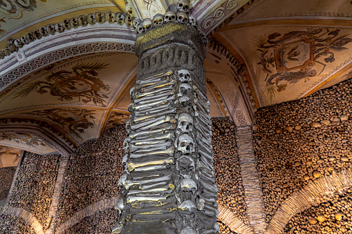 Column covered and decorated with human bones and skulls and the vaulted ceiling with religious allegorical paintings from The Chapel of Bones. Evora, Portugal.