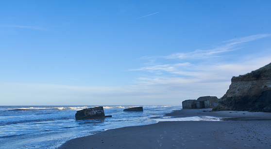 Scenic view of waves reaching towards old ruins and rocks at seashore against blue sky during sunset