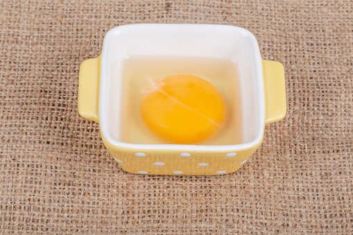 egg yolk, one raw egg yolk in a small yellow bowl on table with copy space. raw food ingredients. food preparation concept background or surface with healthy ingredient on table with copy space