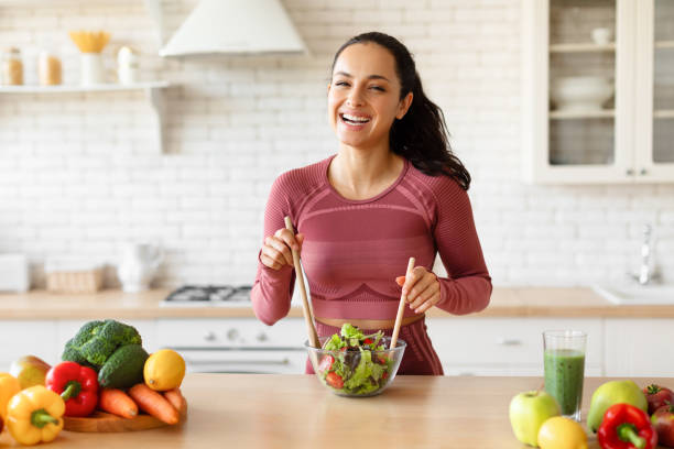 istock Lady in sportswear cooking fresh vegetable salad at kitchen table 1856847837