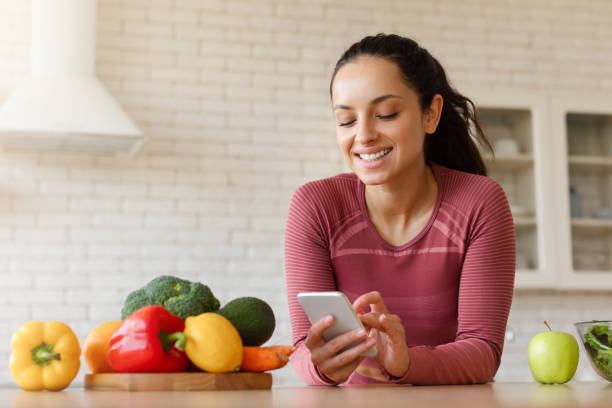 istock Smiling Fit Woman Using Phone With Cooking Application In Kitchen 1856848923