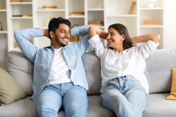istock Happy indian couple on sofa, hands behind head, smiling at each other 1856863047