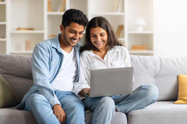 istock Indian young couple browsing on a laptop, seated on sofa at home 1856863128