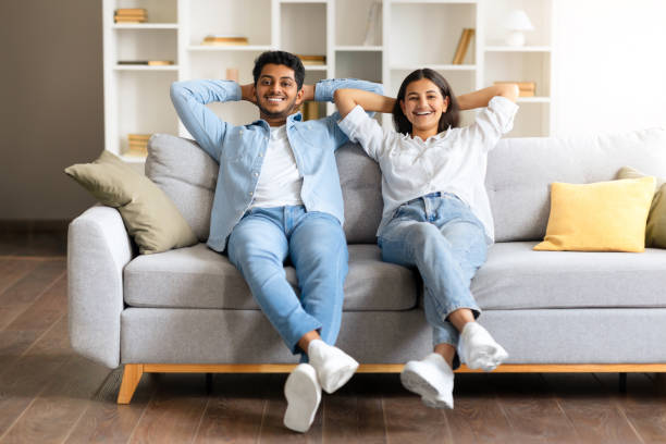 istock Indian young couple relaxing on a sofa with hands behind their heads 1856863595