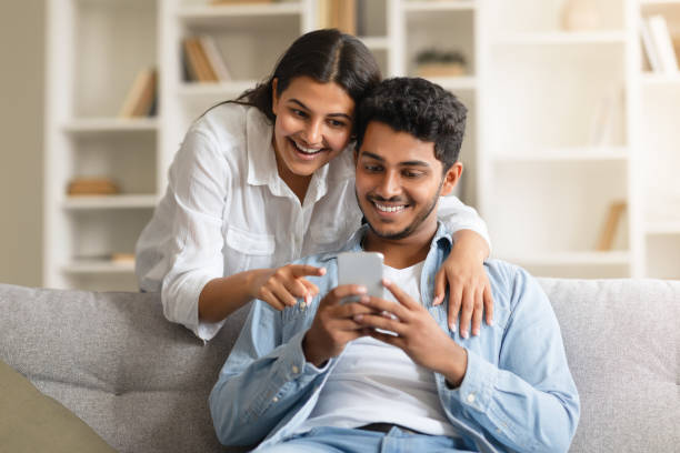 istock Hindu couple sharing a moment, looking at smartphone on couch 1856863596