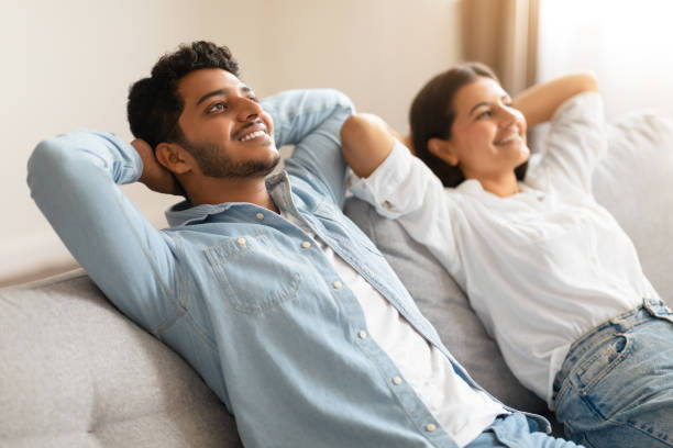 istock Indian couple on sofa, hands behind heads, sharing a joyous moment, both smiling 1856863612