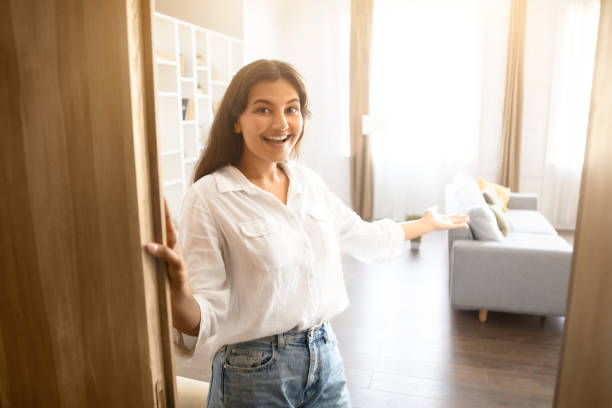 istock Cheerful young Indian woman inviting inside, standing by an open door 1856863614