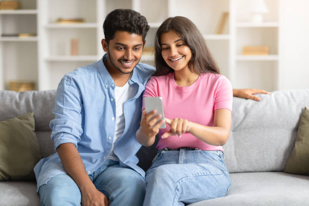 istock Happy Indian couple on sofa using smartphone, woman pointing at phone screen 1856863626
