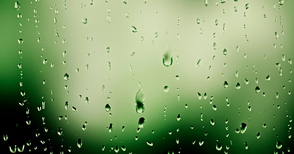 Close-up of raindrops falling on transparent glass window.