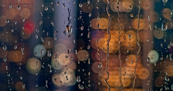 Close-up of illuminated traffic lights and raindrops seen through transparent glass.