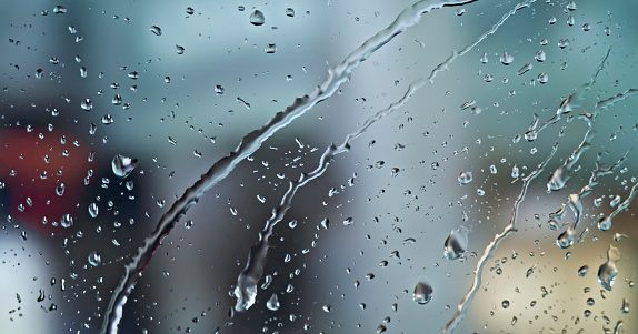 Close-up of water drops falling on transparent glass window.