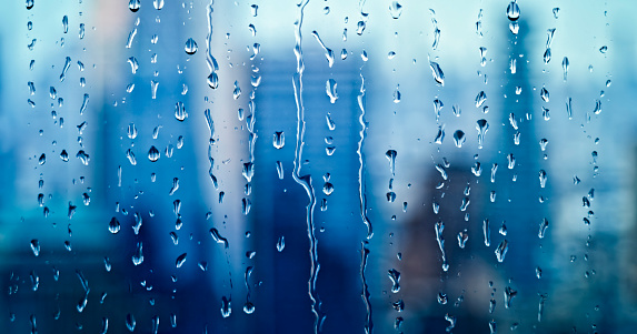 Raindrops on window with clouds.  Blue hue added.