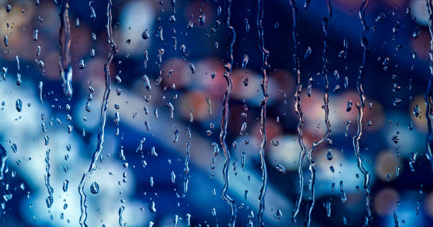 Close-up of illuminated traffic lights and raindrops seen through transparent glass.