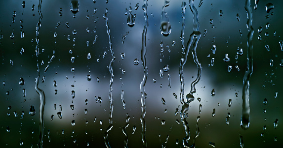 Close-up of water drops falling on transparent glass window.