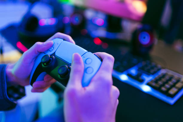 istock Young happy Asian man. Focus on hand holding and pressing buttons of a wireless controller playing a video game in a bedroom with red and blue neon lights at home. Leisure time and esports gamer. 1856870863