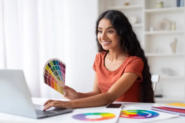 Indian Woman Freelance Graphic Designer Working With Laptop And Color Swatches At Desk In Home Office, Smiling Young Eastern Lady Choosing Color Gamma For New Design Project, Free Space