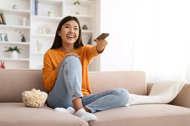 istock Happy young asian lady watching TV and eating popcorn 1856893249