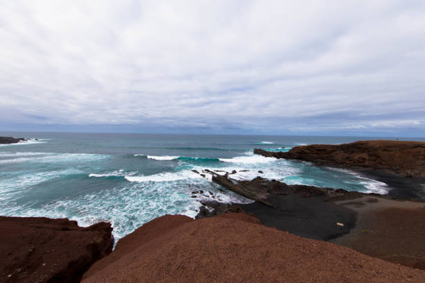 Panoramic view of Playa El Golfo volcanic beach and rocky coast on a windy day. Seen from the Charco de los Clicos viewpoint. Lanzarote, Canary Islands, Spain