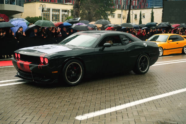 Tirana, Albania - November 28, 2023: On Avenue of Martyrs of the Nation, citizens watch a modified car parade, including a black Dodge Challenger driven by a blonde woman, on a rainy Independence Day