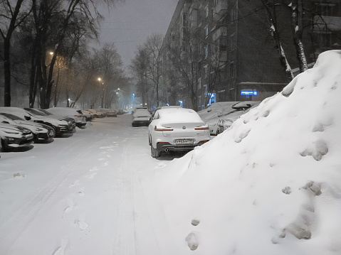 Cars are parked in a city yard among snowdrifts on a winter night. Heavy snowfall in Moscow. Moscow. Russia. December 15, 2023.