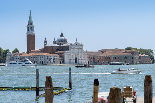 Venice, Veneto, Italy- June 26, 2023; on a sunny summer morning view from a pier of the Basilica Di San Giorgio Maggiore. Tourist boats sail in front of the basilica showing one of Venice's beautiful religious monuments.