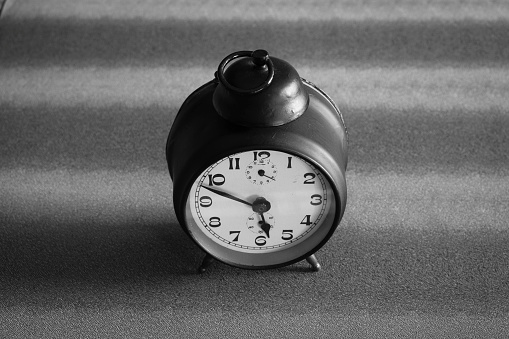 Analog alarm clock, marking a random time, black on gray background