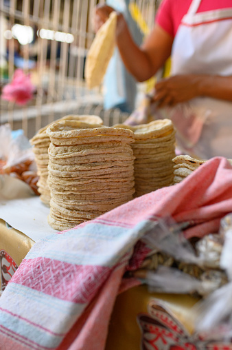 Pile of freshly made tortillas on counter near crop anonymous female cook working at stall in local market during daytime