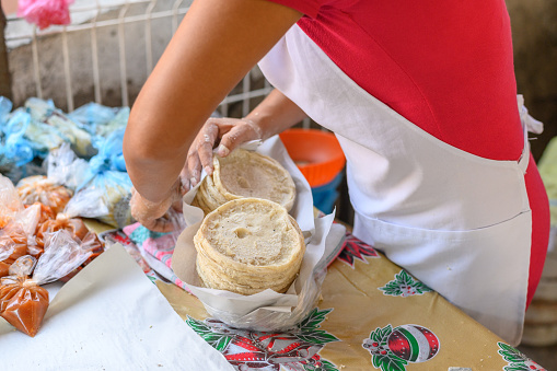 High angle of anonymous female chef in apron standing at table and wrapping tasty Mexican flatbreads into napkins in Mexico