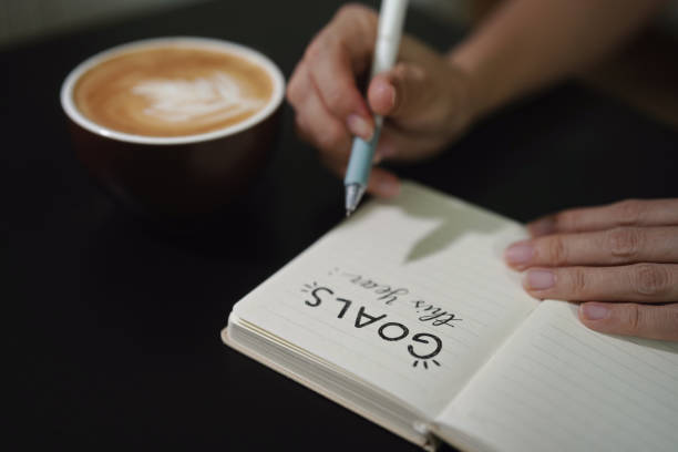 istock Businesswomen writing 'GOALS this year' on a notebook, planning on New Year's Resolutions, coffee cup on desk 1857035061