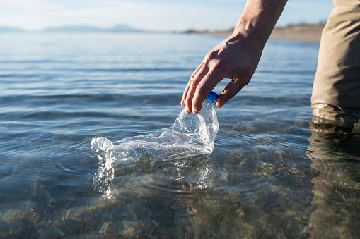 Unrecognizable person cleaning up plastic bottles from the ocean.