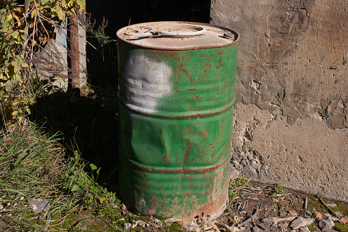 Green rusty metal fuel barrel in abandoned industrial dilapidated buildings.