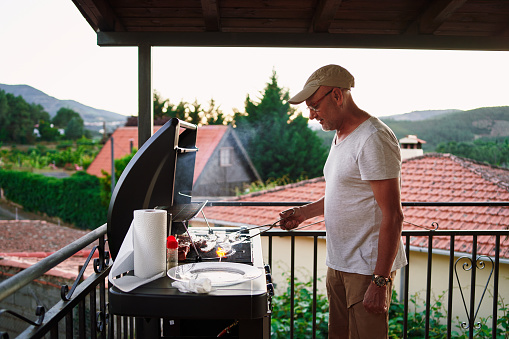 Man cooking meat in a domestic barbecue in the terrace with views of a village