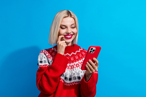 Photo of pretty charming lady finger touch lips think use smart phone texting wear red pullover isolated on blue color background.