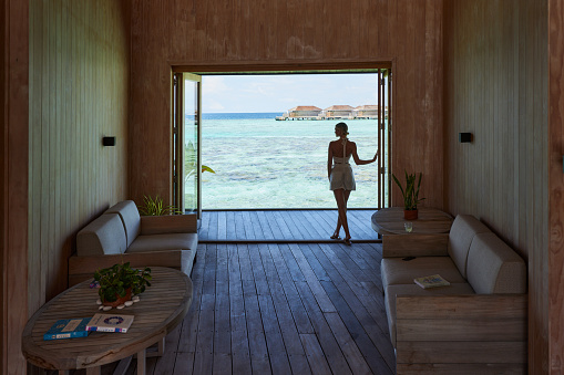 Rear view of carefree woman standing on a patio door from the living room by the sea. Copy space.