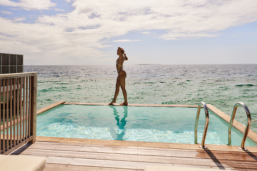 Young woman walking at the edge of a swimming pool by the sea. Copy space.
