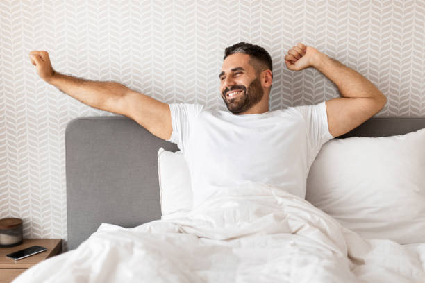 istock man smiling and stretching arms while sitting up in bed 1857087051