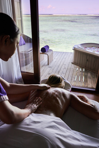 Massage therapist giving her customer a relaxing back massage at the spa in a tourist resort by the sea.
