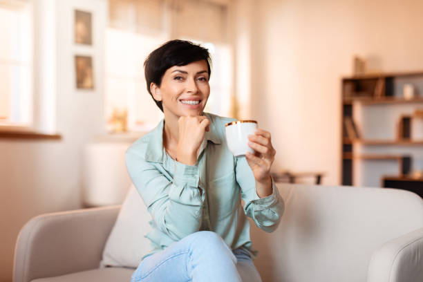 istock Middle aged woman enjoying hot tea sitting on sofa indoor 1857117935
