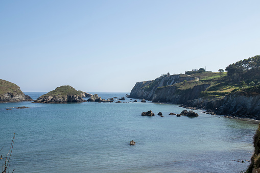 tranquil coastal scene with clear blue waters, rocky islets, lush cliffs, and a bright, inviting sky