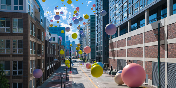 An abstract image of large multi-coloured balloons or spheres falling onto an empty city street in downtown high street location with large buildings on a bright sunny day.