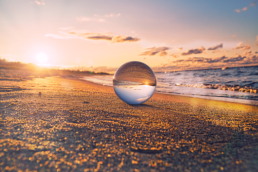Glass globe on the beach of the Baltic Sea in Zingst in which the landscape is depicted. The sunset provides a warm light mood